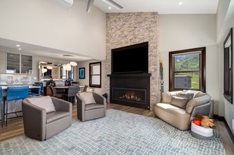 A bright and open living area at Torian Plum Plaza 803 with a stone fireplace, cozy armchairs, and a view of the green mountain landscape outside.