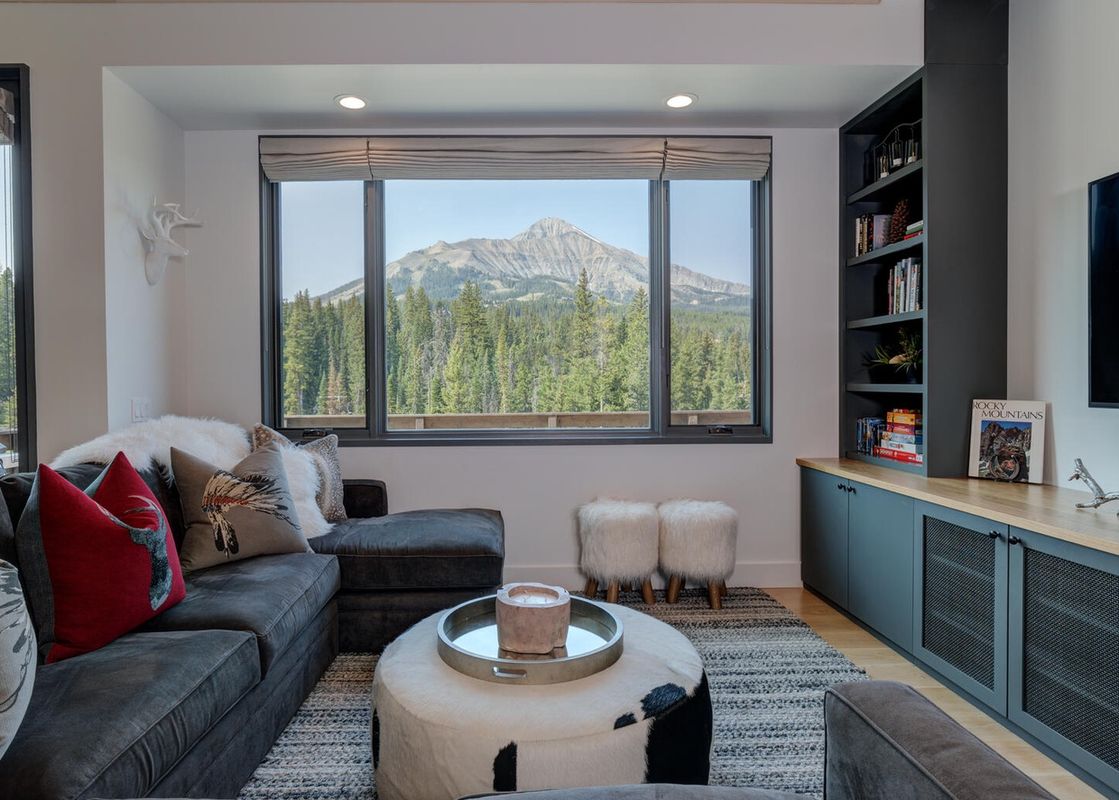 Moonlight Basin 17 Lake Cabin features a spacious living area with a large sectional sofa, a cozy fireplace, and a stunning view of the mountains.