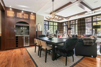 The dining area in Flagstaff 204 features a dark wood dining table, antler chandelier, and a wet bar with wine storage, offering views of the outdoors through large windows.