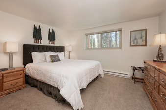 The bedroom at Beaver Village 514 features a plush bed with an upholstered headboard, bedside tables, and rustic decor, offering a cozy and inviting retreat.