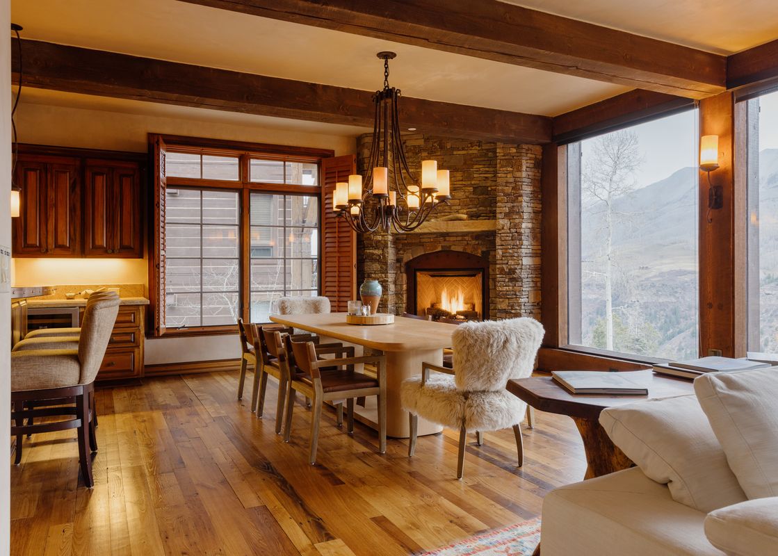 A spacious dining and living area featuring a large wooden dining table, a cozy fireplace, and a window with a mountain view.