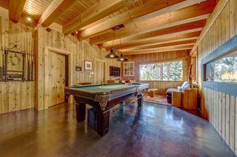A rustic games room featuring a pool table under exposed wooden beams and wood-paneled walls.