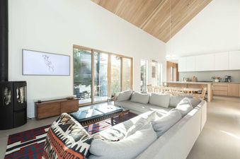 A modern and bright open-concept living area at Serenity Domain with high wood ceilings, a large grey sectional, and sliding doors showing an exterior view.