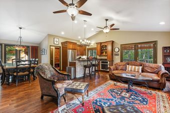 A spacious great room at Scouts Retreat featuring a kitchen with wooden cabinetry, a dining area with a large table, and a living room with a leather sofa and a patterned rug, all bathed in natural light from large windows.
