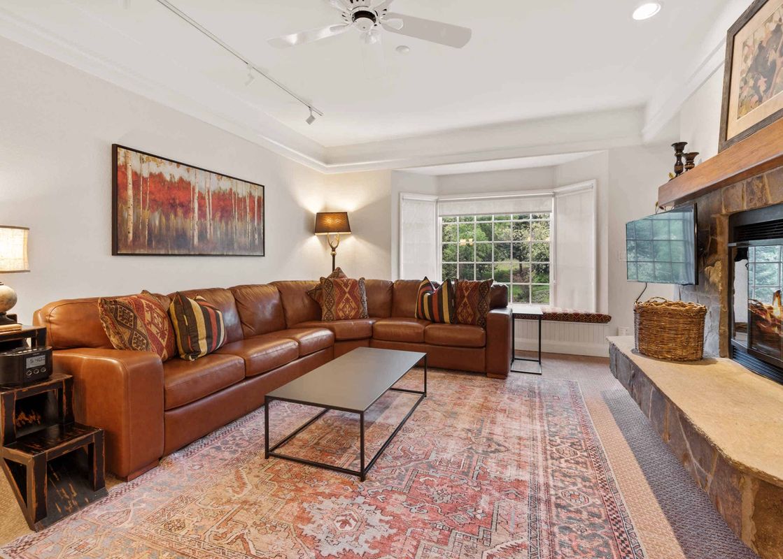 The living room at The Charter B3305 featuring a brown leather sectional, a patterned area rug, a modern coffee table, and a fireplace.