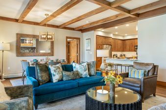 Inviting open-concept living area at 304C Bear Paw Lodge featuring a teal sofa, wooden ceiling beams, dining area, and kitchen view.