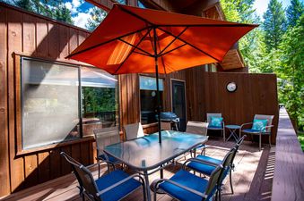A private outdoor deck at The Cedar Nest, featuring a dining table, chairs, and a large orange umbrella, set amidst lush greenery.