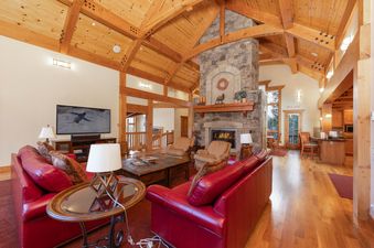 The living area of Timber Trail Lodge features a large stone fireplace, red leather sofas, and a high vaulted wooden ceiling, creating a cozy and luxurious atmosphere.