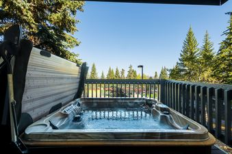 A private hot tub on a balcony, surrounded by lush trees and offering a view of a tennis court in the distance.
