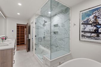 A modern bathroom with a walk-in marble shower, a double vanity, a freestanding tub, and a large framed artwork.