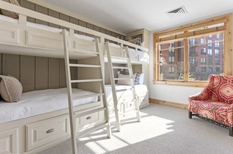 A bright bunk bedroom in Silver Strike Lodge 302 with custom bunk beds, white bedding, a large window, and a colorful armchair.