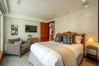 A cozy bedroom with a large bed, a comfortable armchair, and a flat-screen TV.