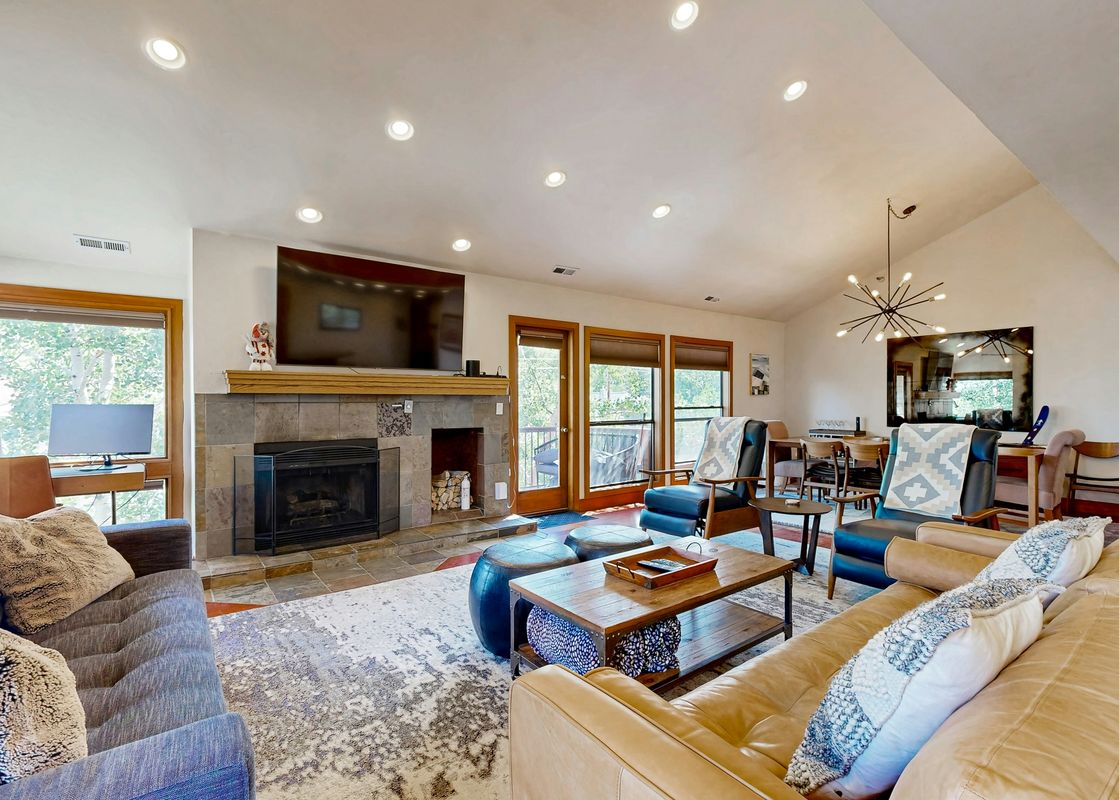 The living area of Silver Cliff Village 205 features a large fireplace, a television, and comfortable seating, with multiple windows offering views of the lush outdoors.