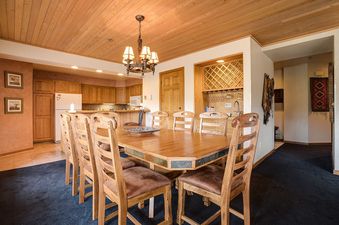 An inviting dining area at Chateau Chamonix CX122 with an octagonal wooden table and matching chairs, set against a backdrop of a fully equipped kitchen and a built-in bar.