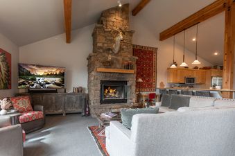 Cozy living area in Moose Creek 1 featuring a dramatic stone fireplace, comfortable sectional sofa, and kitchen in the background.