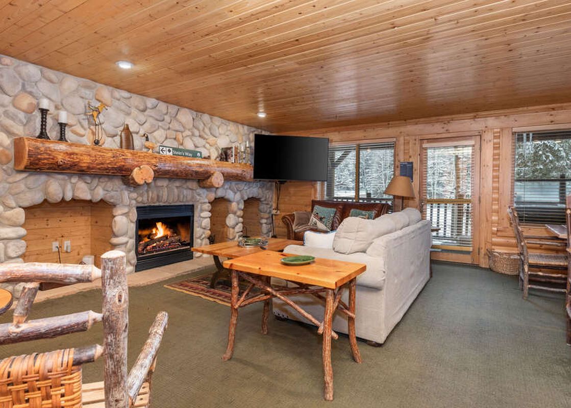 A cozy living room inside Black Bear 204 with a stone fireplace, wooden tables, and comfortable seating.