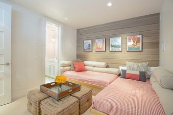 A bedroom with two twin beds, a wood accent wall with framed posters, a small tray table, and a door to a bathroom in the background.