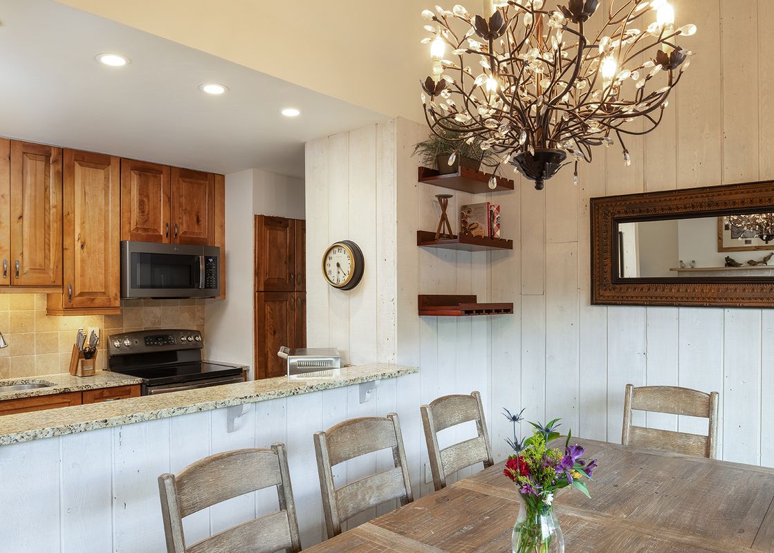 A bright open-concept kitchen and dining area at Vantage Point 504 featuring wooden cabinetry, granite countertops, and a dining table with a decorative chandelier above.