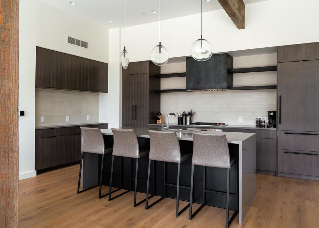 The modern kitchen in Moonlight Basin 212 Lakelodge features sleek dark cabinetry, stainless steel appliances, a breakfast bar with four bar stools, and a spacious island countertop.