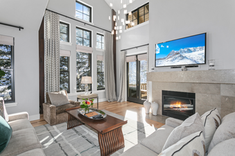 The living room of the Lodges at Deer Valley 2 Bedroom Suite features a large flat-screen TV above a fireplace, two large comfortable couches with plush pillows, and a coffee table with a vase of flowers.