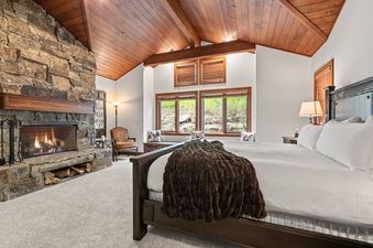 A luxurious bedroom at Slopeside Deer Valley with a large stone fireplace, a cozy bed, and rustic wooden vaulted ceilings.