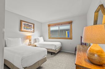 A cozy twin bedroom at Snow Flower 41 Park City featuring two beds, a nightstand with a lamp, and a framed fish artwork above the bed.