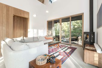 A modern and cozy living area at Serenity Domain featuring a large gray sectional, a wood-burning fireplace, and sliding doors opening to a scenic deck.