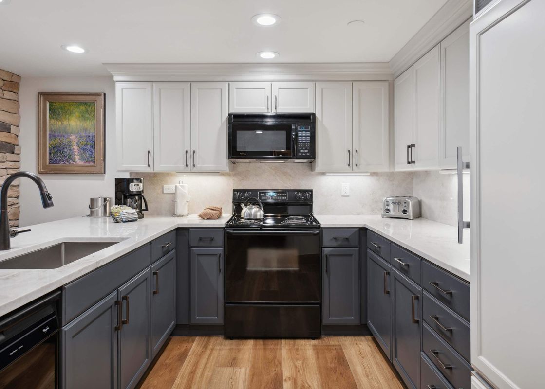 A modern kitchen in The Charter L223 featuring grey and white cabinetry, white marble countertops, and black appliances.