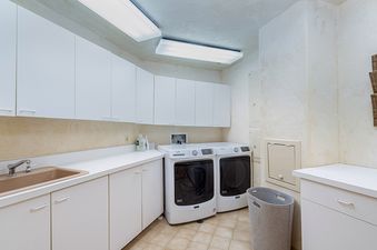 A white laundry room with a washer and dryer, a sink, and cabinets.