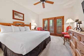 A serene bedroom in The Charter C0105 with a large bed, wooden furniture, red accent chairs, and glass doors leading to an exterior view.