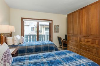 The bedroom at Plaza Lodge 3 Bedroom Gold Unit 4 features two comfortable beds with blue plaid comforters, a large window offering a view of the outside, and a built-in wooden wardrobe with a desk area.