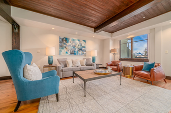 Relax in the living room of Lumiere One Bedroom Deluxe Residence, which features a plush sofa, comfortable chairs, and a warm, inviting atmosphere. Enjoy the views of the snowy mountain peaks from the large windows.