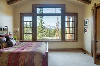 A king-size bed with a striped bedspread in a bedroom with a large window offering mountain and forest views.