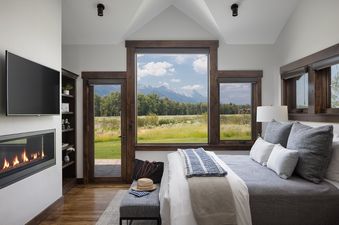 A cozy bedroom with a stunning mountain view features a large bed, a modern fireplace, and expansive windows.