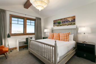 The bedroom in Grand Lodge Four Bedroom 302 features a king-size bed with orange and white patterned pillows and a view out the window.