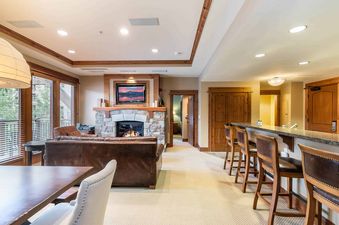 A living room with a fireplace, a leather couch, a dining table, and a kitchen bar with stools.