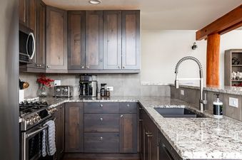 The kitchen of Moonlight Basin Saddle Ridge D1 features a granite countertop, stainless steel appliances, and dark wood cabinets.