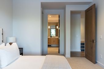 The bedroom at Moonlight Basin 7 Speedwell Drive has a king-size bed and large windows. The bedroom is decorated with a white bedspread and a modern, minimalist style.