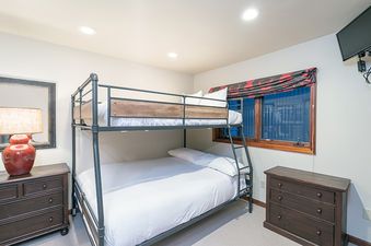 A bedroom with a bunk bed, dresser, and a window.