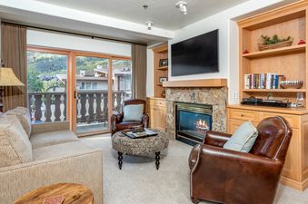 The inviting living area of Bridge Street Lodge 1 Bedroom Platinum Unit 301 features a cozy fireplace, comfortable seating, and a large sliding glass door leading to a balcony with scenic mountain views.