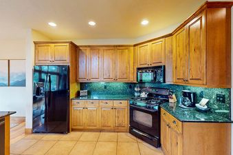 A fully equipped kitchen with wooden cabinetry, black appliances, and dark green countertops at EagleRidge Townhomes 1510.