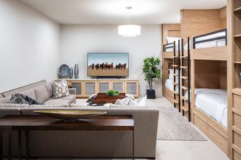 Moonlight Basin 83B Lodgeside has a large sectional sofa and a flat-screen TV in the living room. There is a bunk bed in the hallway and a coffee table with a brown leather top.