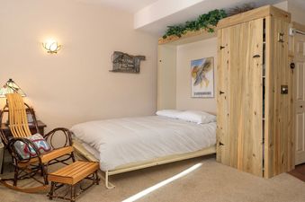 A cozy bedroom with a Murphy bed, a rustic wooden rocking chair, and warm lighting.