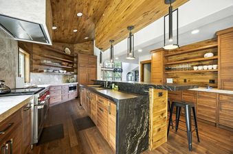 A modern kitchen with wooden cabinetry, a large island with black and white granite, and sleek pendant lights.