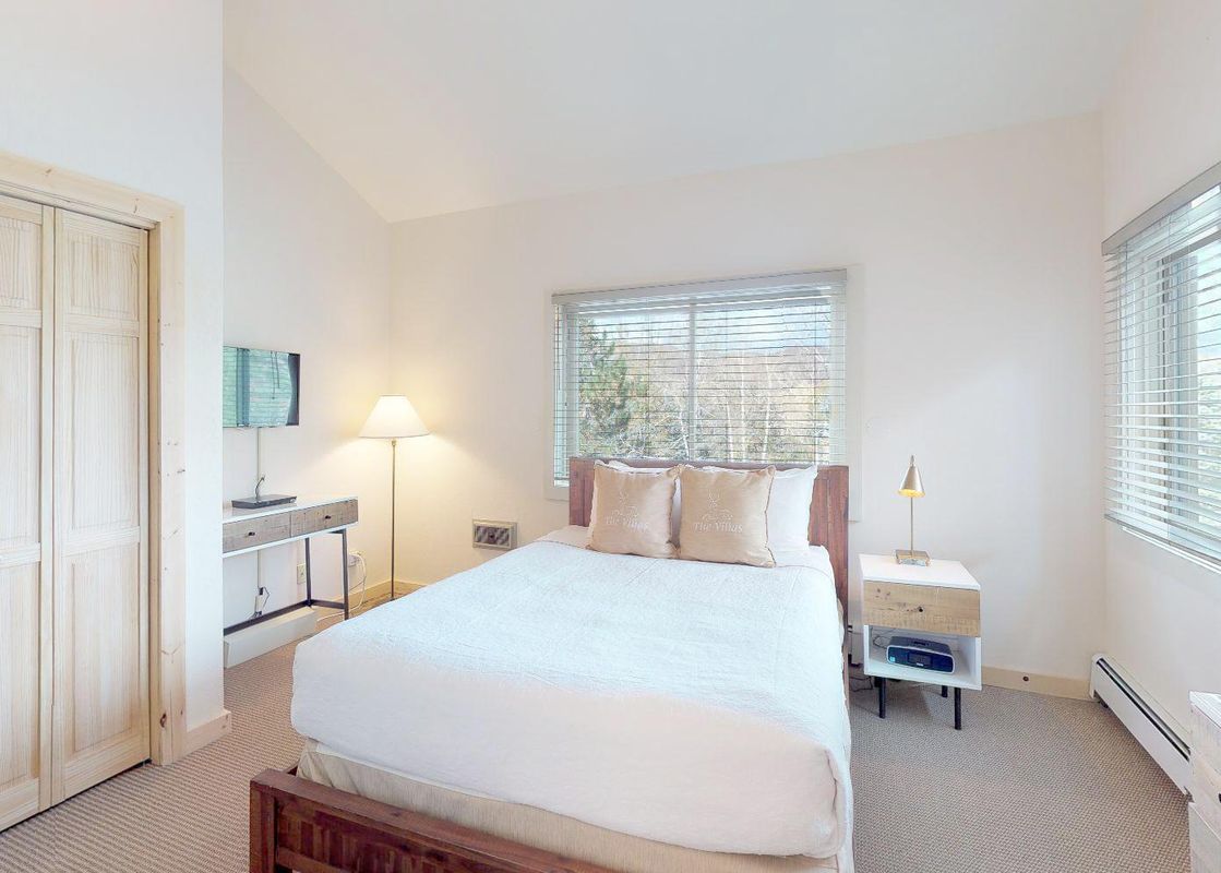 A cozy bedroom in Villas at Snowmass Club L1433 features a comfortable bed with beige pillows, a large window with blinds, and light wooden furniture.