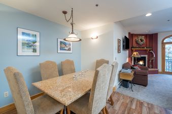 Dining table with chairs in a well-lit, spacious room, with a fireplace in the background.