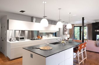 A modern kitchen at Riverbend House with white cabinets, dark countertops, a stainless steel backsplash, and a kitchen island with orange bar stools.