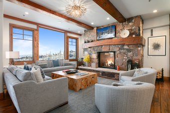 The spacious living area in Grand Lodge Three Bedroom Deluxe 408 features a stone fireplace with a roaring fire, comfortable couches, and a large coffee table.