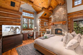 A rustic bedroom at Timber Ridge at Jackson Hole with a king bed, log walls, and a large stone fireplace.