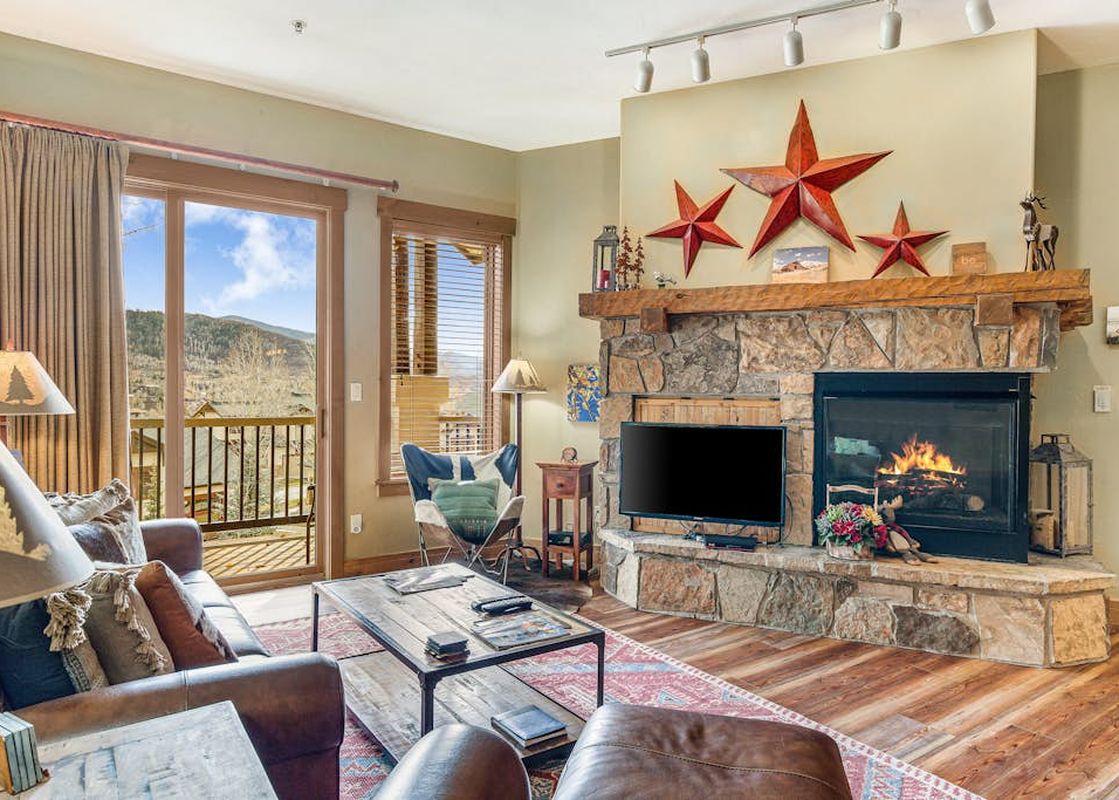 Inviting living room in EagleRidge Lodge 306 featuring a stone fireplace with a burning fire, leather sofa, and mountain views.
